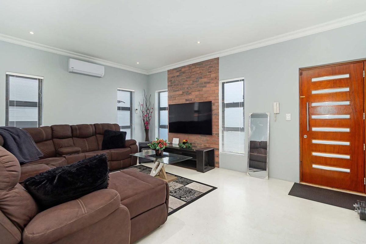 Spacious living room featuring an exposed brick feature wall, split-system air conditioning, recessed lighting, and a solid timber front entrance door.