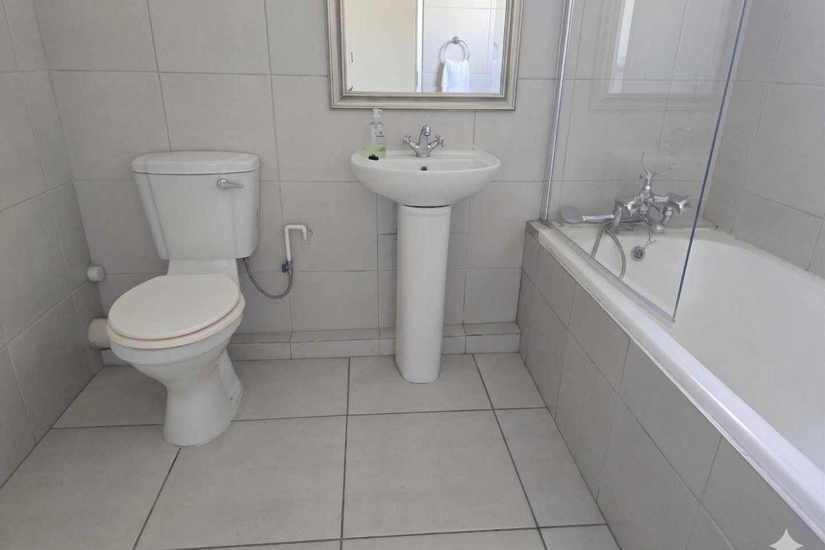 A functional bathroom featuring a pedestal basin, a standard toilet, and a bathtub with a glass shower screen and wall-mounted mixer.