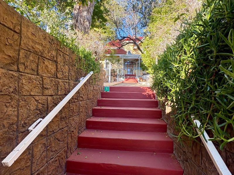 An exterior view of a property entrance featuring a set of painted concrete stairs flanked by stone retaining walls and metal handrails.