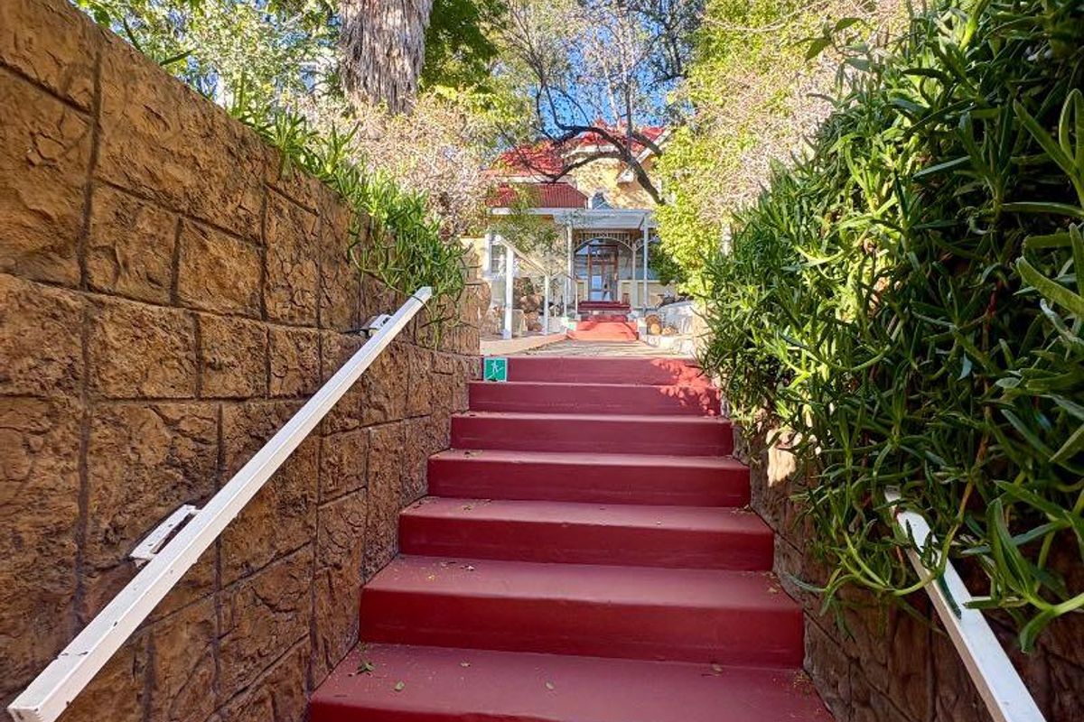 An exterior view of a property entrance featuring a set of painted concrete stairs flanked by stone retaining walls and metal handrails.