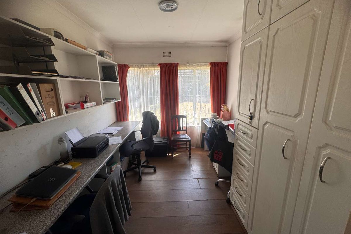 A functional bedroom or home office featuring built-in cabinetry, a desk, and shelving, with security bars on the window.
