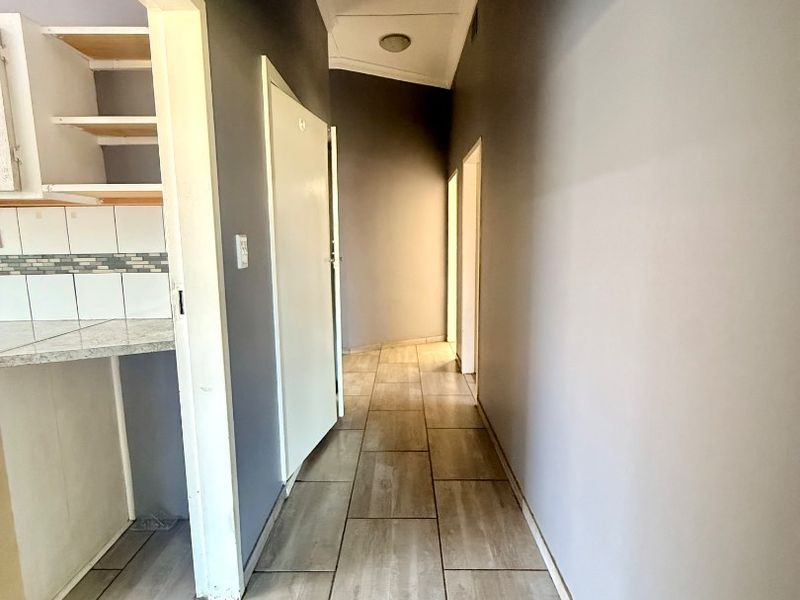 A neutral-toned hallway featuring modern tiled flooring and recessed lighting, providing access to adjacent rooms including a partially visible kitchen area.