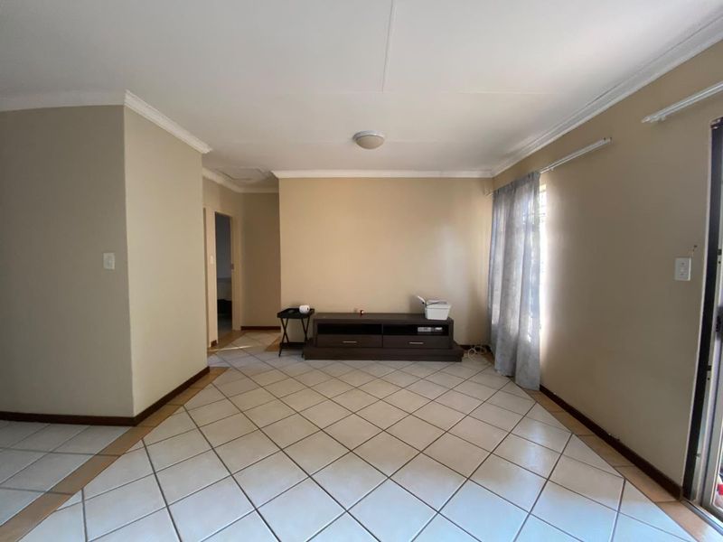 A spacious, neutrally painted living room featuring ceramic floor tiles, coving, and a sliding glass door providing natural light.
