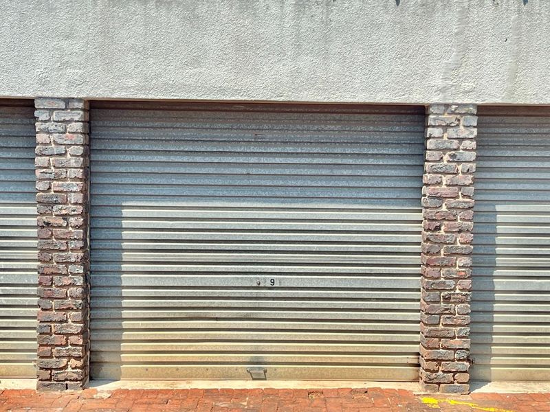 A secure metal roller garage door featuring exposed brick pillars and a stucco facade finish.