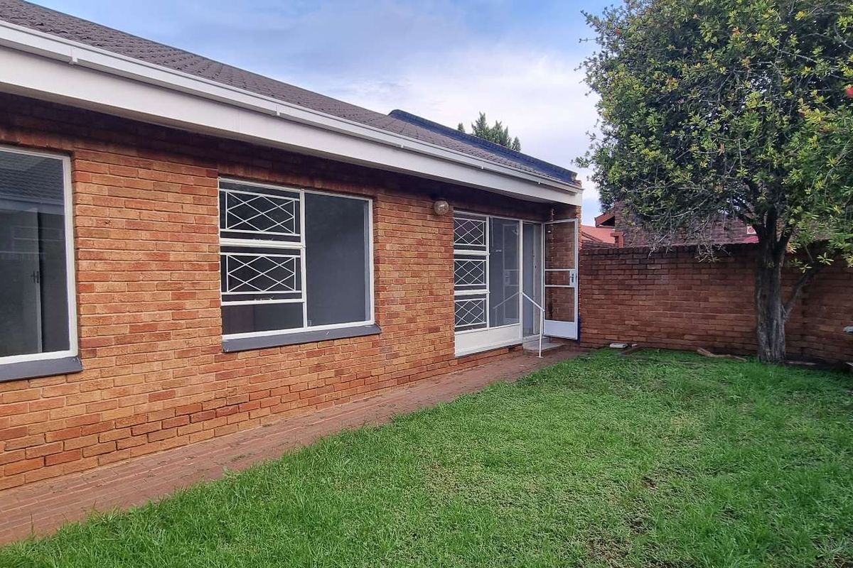 Rear view of the townhouse featuring a face-brick exterior, security-barred windows, a paved walkway, and a private garden area.