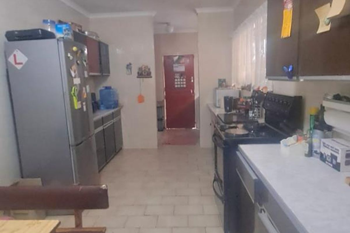 A functional kitchen featuring laminate countertops, dark cabinetry, and tiled flooring, leading through to an exterior entrance door.