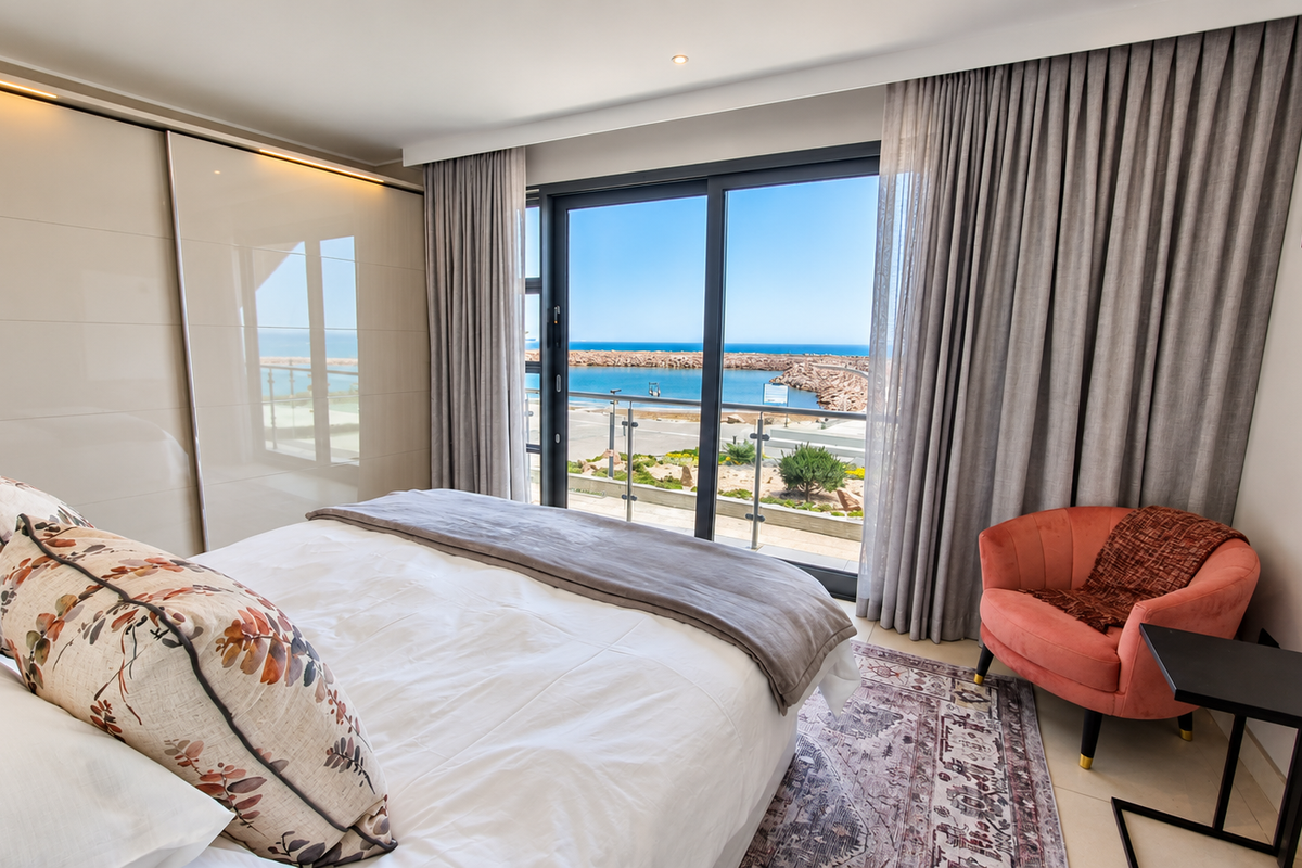Modern bedroom featuring a built-in wardrobe and large sliding glass doors opening to a balcony with scenic coastal and harbour views.