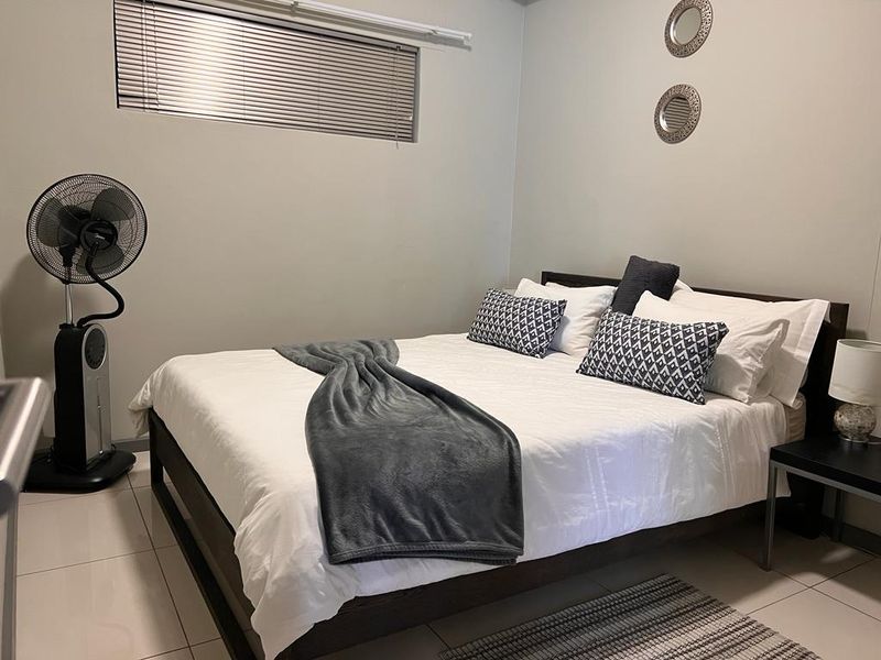 A well-maintained bedroom featuring neutral wall tones, tiled flooring, and a window fitted with venetian blinds.