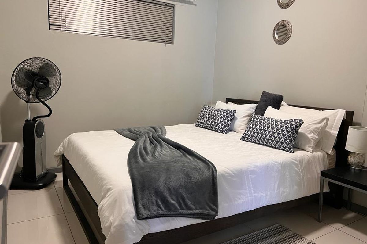 A well-maintained bedroom featuring neutral wall tones, tiled flooring, and a window fitted with venetian blinds.