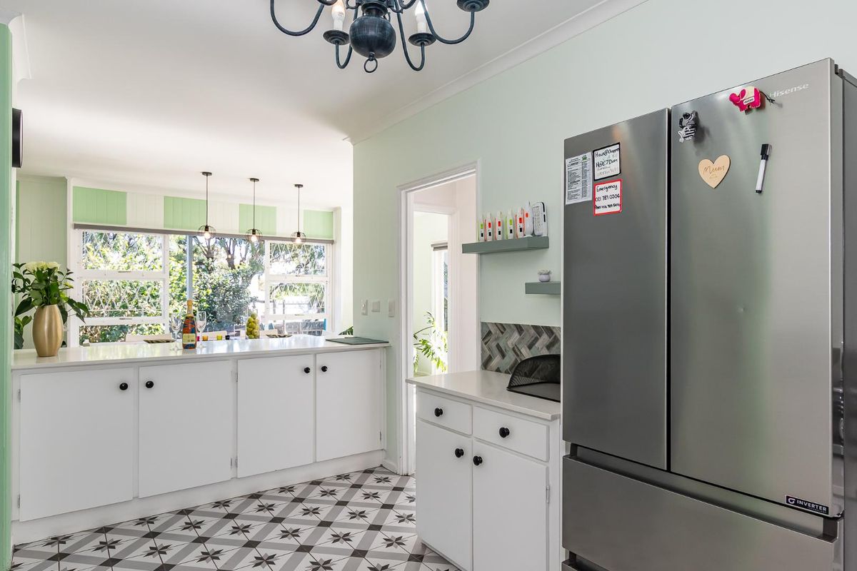A bright kitchen featuring white cabinetry, stone countertops, a stylish herringbone backsplash, and patterned floor tiles, complemented by modern pendant lighting.