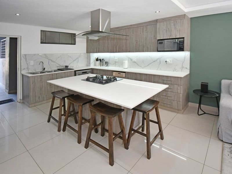 Modern open-plan kitchen featuring a central island with gas hob, sleek cabinetry, marble-look splashback, and integrated appliances, seamlessly flowing into the living area.