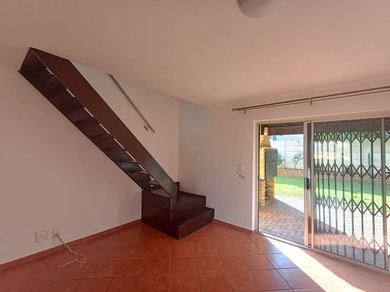 An open-plan living area featuring a wooden staircase, tiled flooring, and sliding glass doors providing direct access to a patio with a built-in braai.