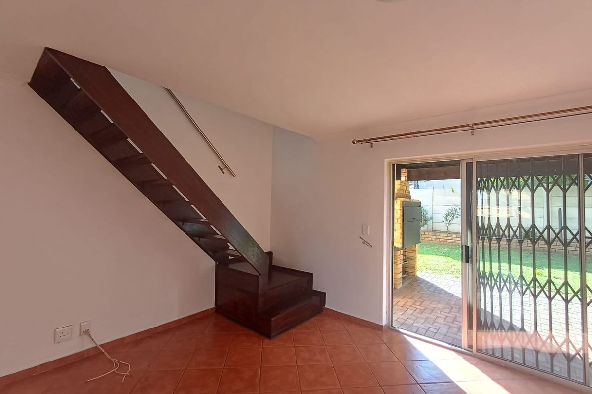 An open-plan living area featuring a wooden staircase, tiled flooring, and sliding glass doors providing direct access to a patio with a built-in braai.