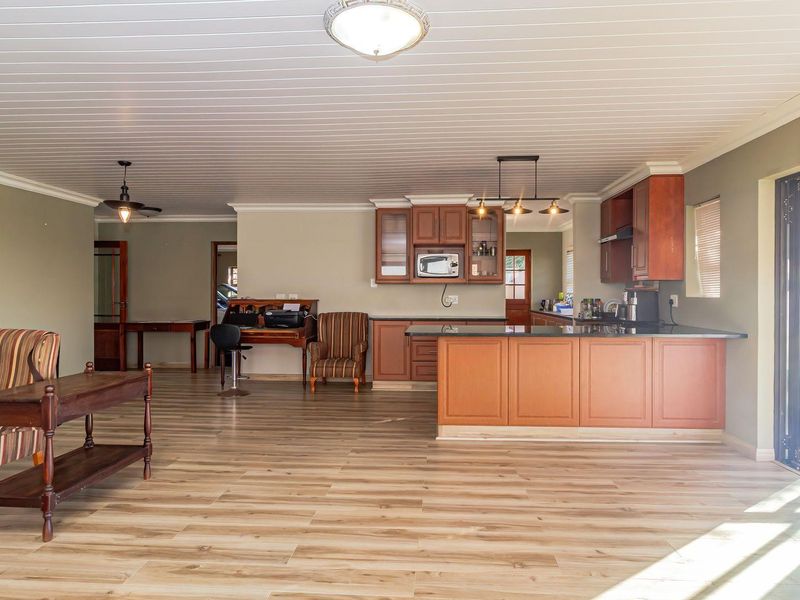 Spacious open-plan living and kitchen area featuring warm-toned cabinetry, a central island, modern laminate flooring, and large sliding doors leading to the outdoors.