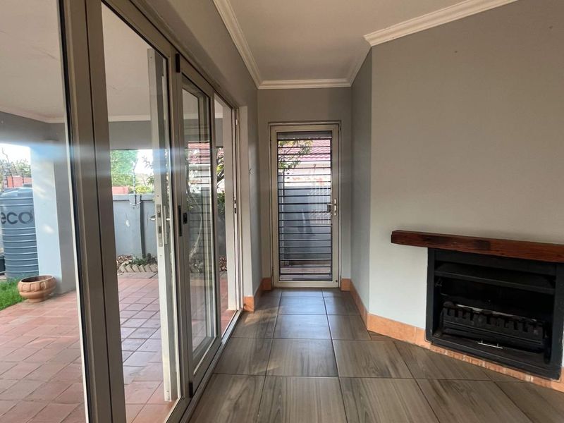 A covered patio area featuring tiled flooring, a built-in fireplace with a wooden mantel, and large sliding glass doors leading to the garden.