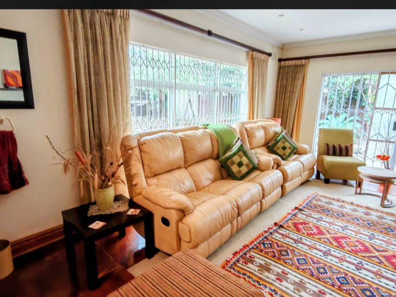 A comfortable living room featuring hardwood flooring, recessed lighting, and large windows with security gates, providing access to the outdoor area.