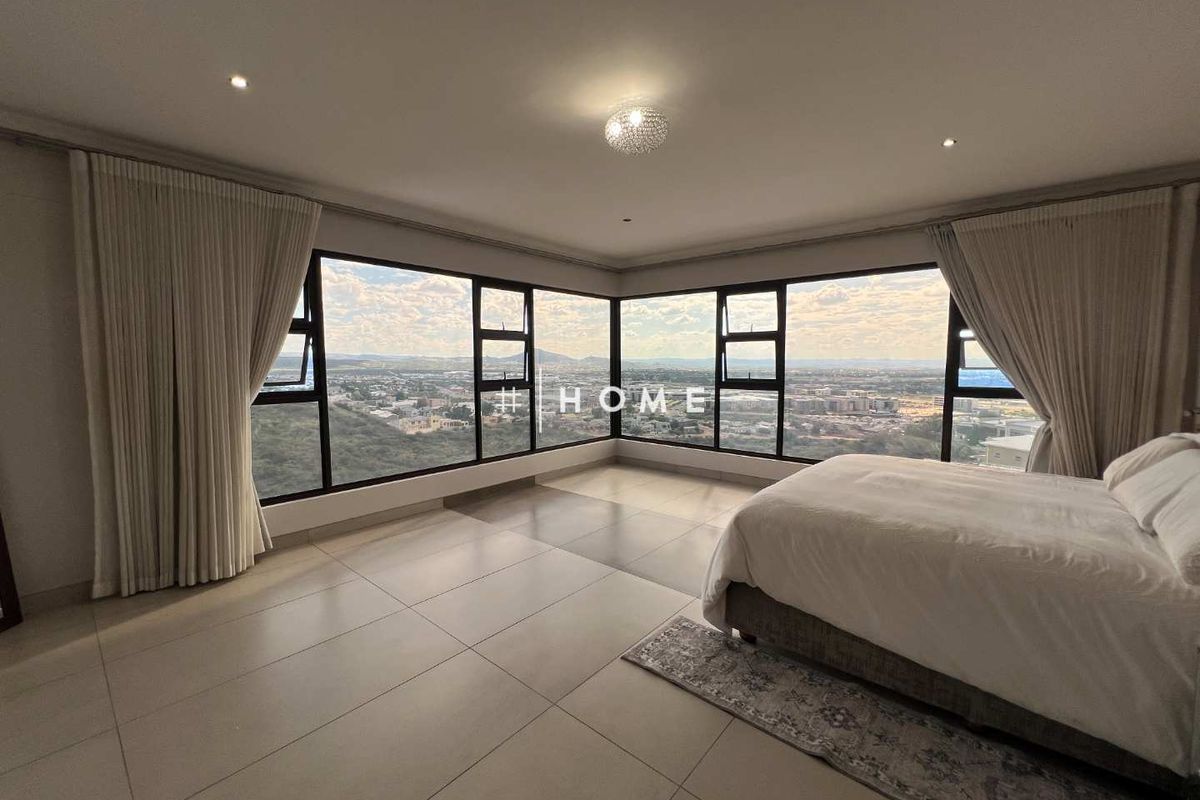 Spacious bedroom featuring expansive corner windows with panoramic city views, tiled flooring, and recessed ceiling lighting.