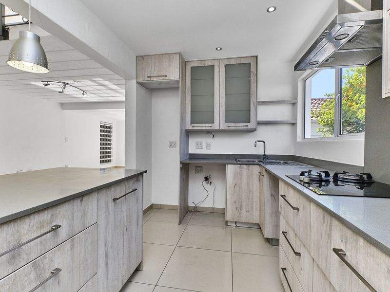Modern kitchen featuring light wood-grain cabinetry, stone countertops, a gas hob with extractor fan, and tiled flooring in an open-plan layout.