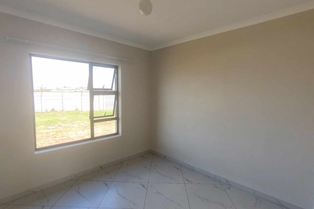 A bright, empty bedroom featuring neutral wall paint, tiled flooring, and a large window providing natural light and a view of the exterior.