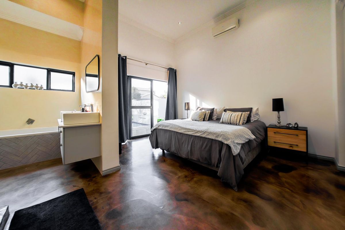 Spacious bedroom featuring an open-plan en-suite bathroom, polished concrete floors, built-in cupboards, and direct access to an outdoor area via sliding glass doors.
