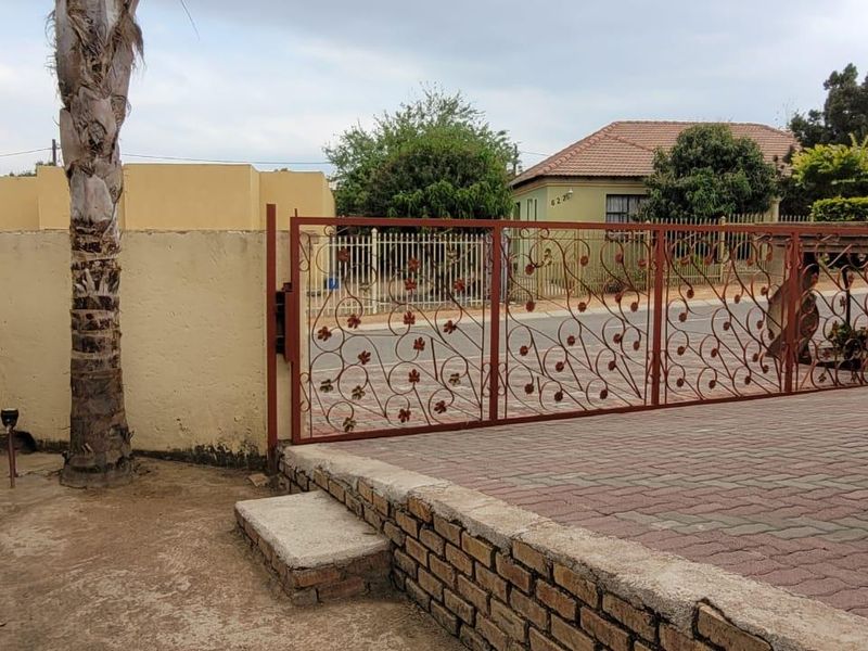 Front entrance area featuring a decorative wrought iron gate, paved driveway, and brick boundary wall.
