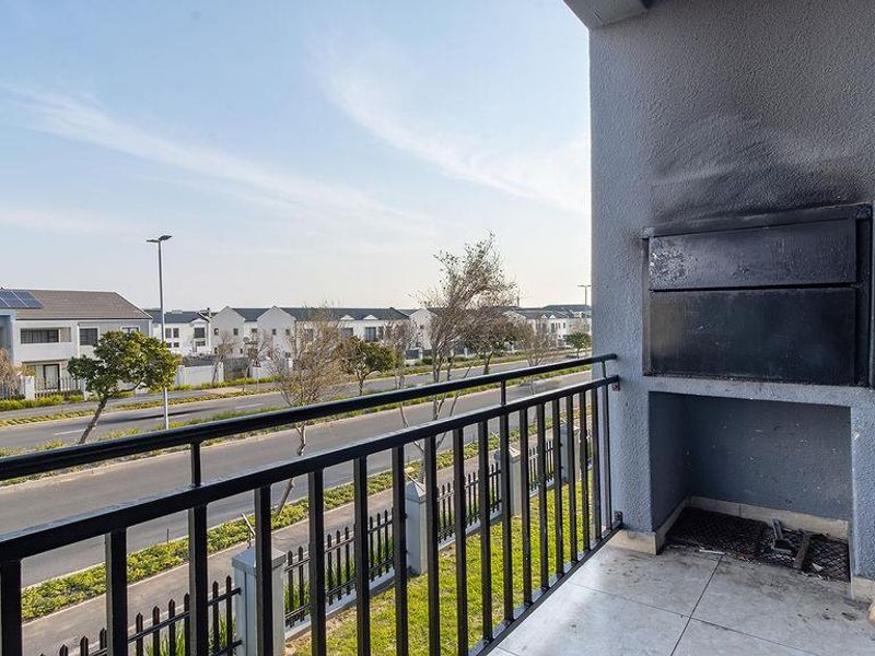 A balcony featuring a built-in braai, metal balustrade, and tiled flooring, offering an open view of the surrounding residential area.