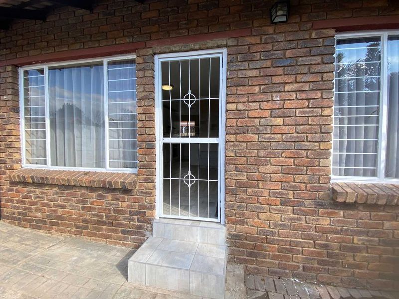 A rear exterior view of the townhouse featuring a face-brick facade, security gate, and tiled entrance step.