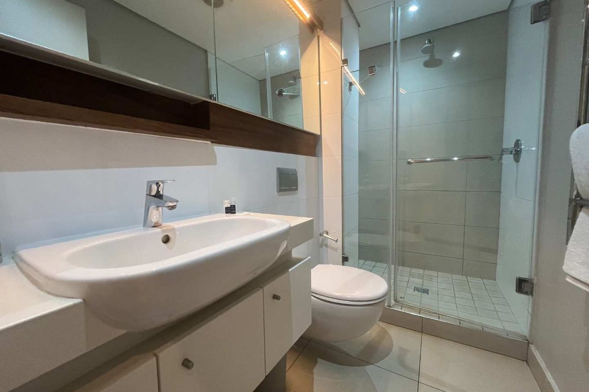 Modern bathroom featuring a wall-mounted vanity with integrated basin, a glass-enclosed walk-in shower, and contemporary tiled finishes.
