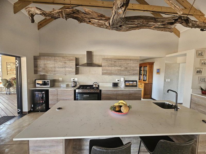 Modern kitchen featuring a large central island with stone countertop, gas stove, extractor fan, and exposed timber beams under a vaulted ceiling.
