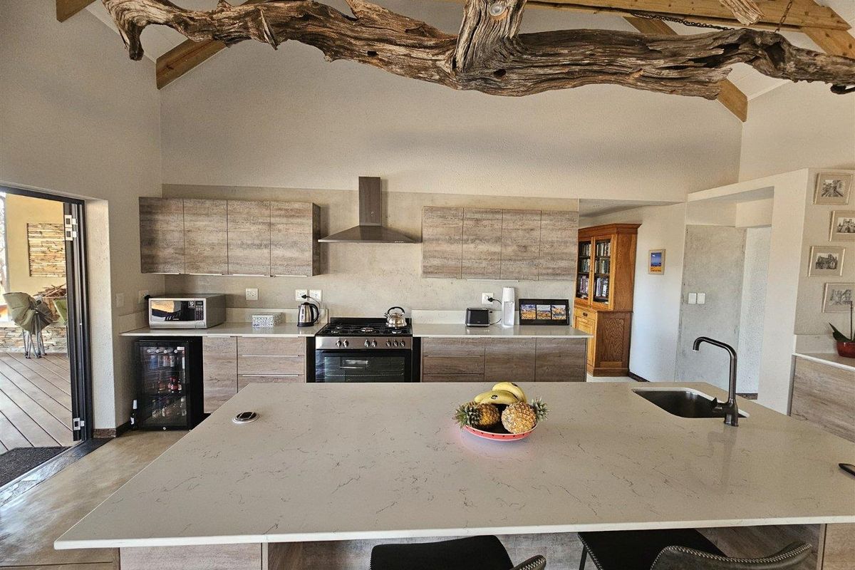 Modern kitchen featuring a large central island with stone countertop, gas stove, extractor fan, and exposed timber beams under a vaulted ceiling.