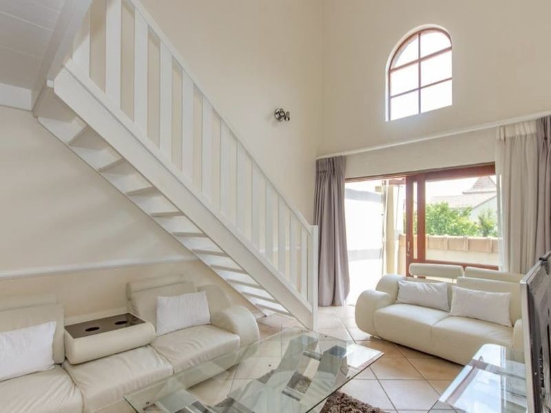 Spacious living room featuring high ceilings, a staircase, tiled flooring, and an arched window providing natural light with access to an outdoor area.
