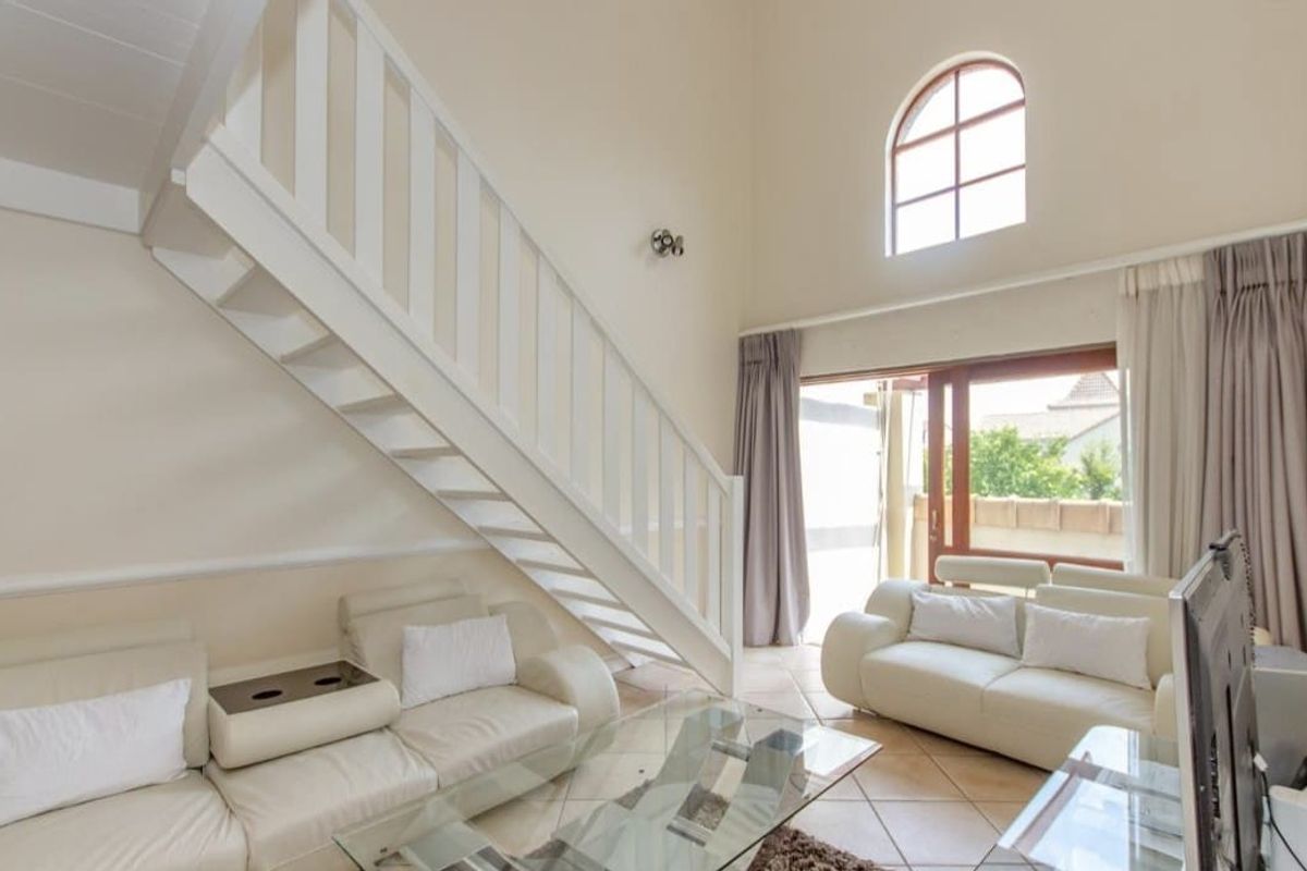 Spacious living room featuring high ceilings, a staircase, tiled flooring, and an arched window providing natural light with access to an outdoor area.