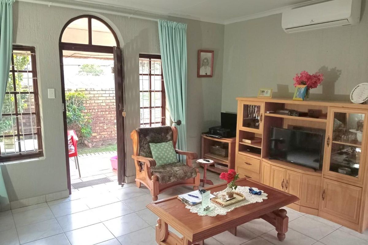 A living room featuring tiled flooring, an arched door leading to the patio, and a wall-mounted air conditioning unit.