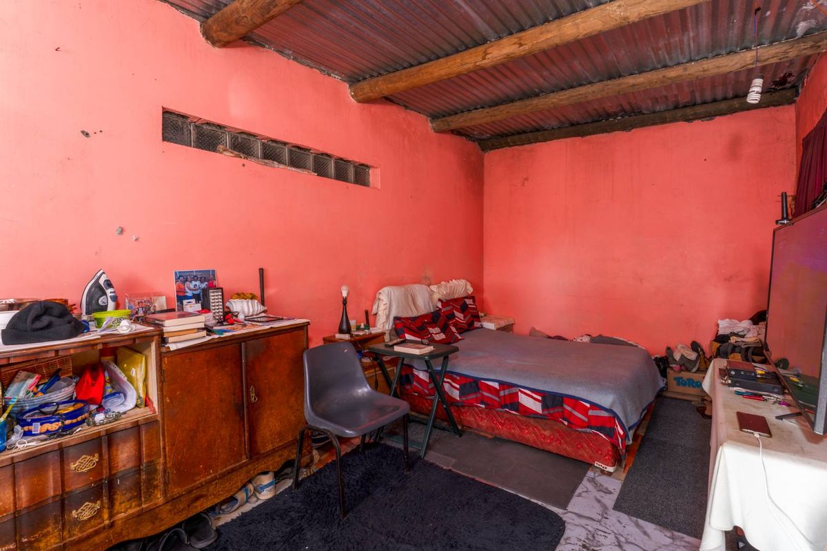 A bedroom featuring exposed timber beams and corrugated metal roofing with a high-set glass block window.