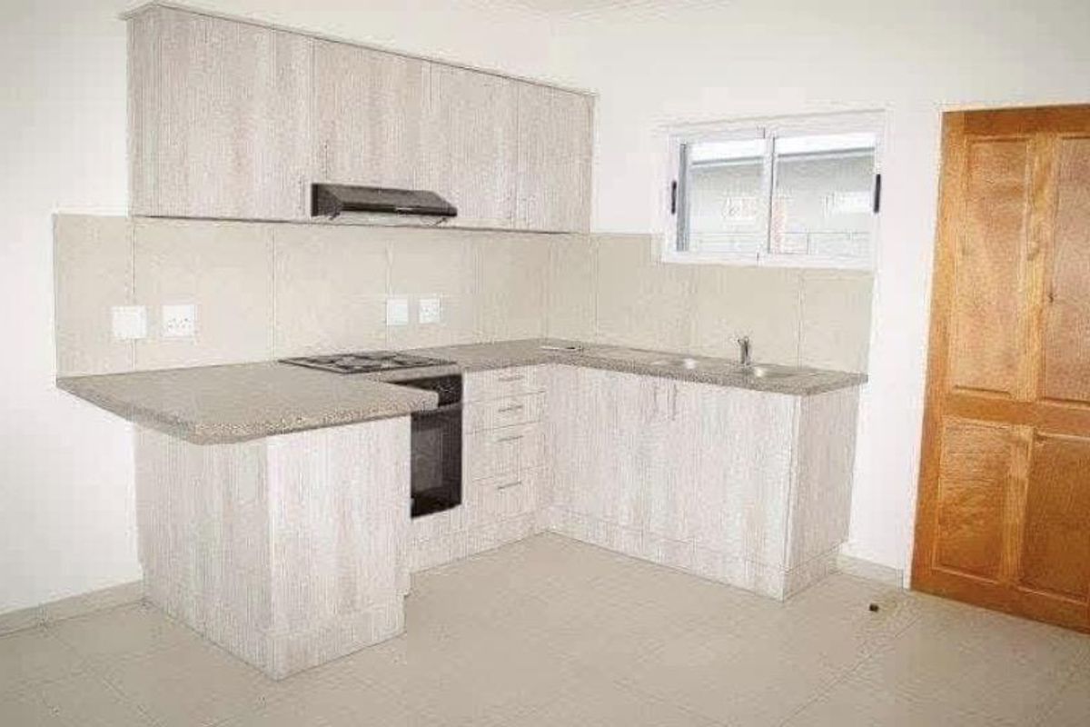 A clean, modern kitchen featuring light wood-grain cabinetry, integrated appliances, tiled backsplash, and neutral floor tiles in an open-plan layout.