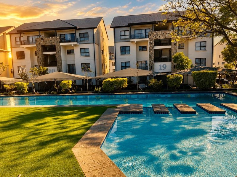 A well-maintained apartment complex pool area featuring a swimming pool, artificial lawn, and modern building facades with stone accents and balconies.
