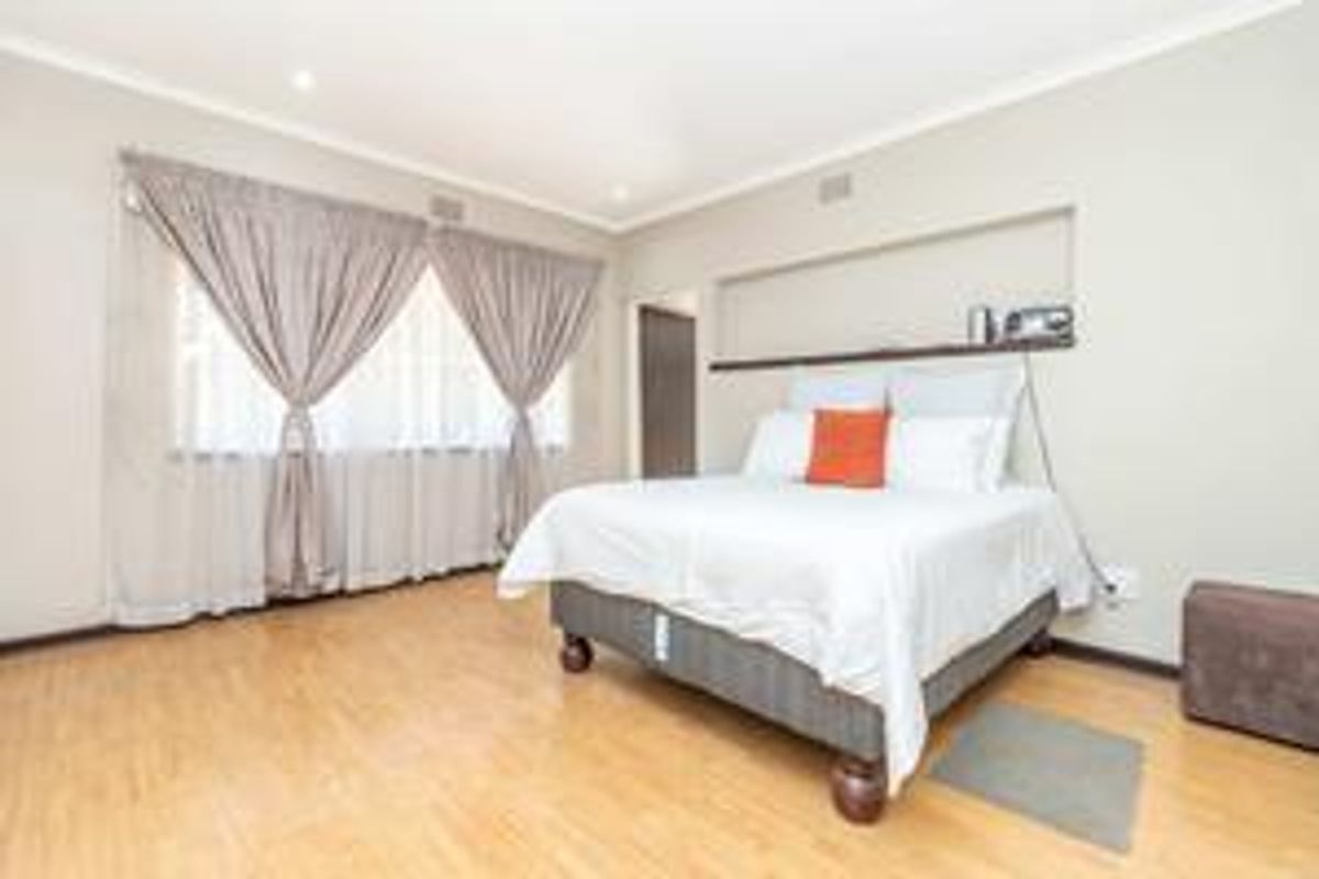 A spacious bedroom featuring light wood-look flooring, recessed wall shelving, and large windows with neutral curtains, providing a bright and comfortable living space.