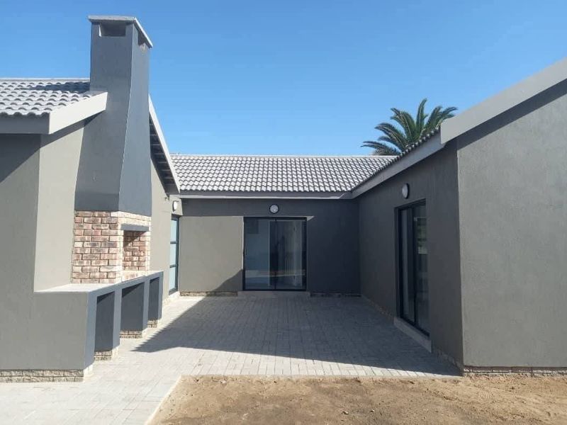 A modern paved patio area featuring a built-in brick braai, chimney, and sliding glass doors providing access to the home's interior.