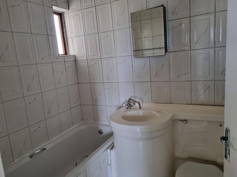 A compact bathroom featuring a built-in bathtub, integrated vanity basin, and wall-mounted mirror cabinet with classic white tiled walls.