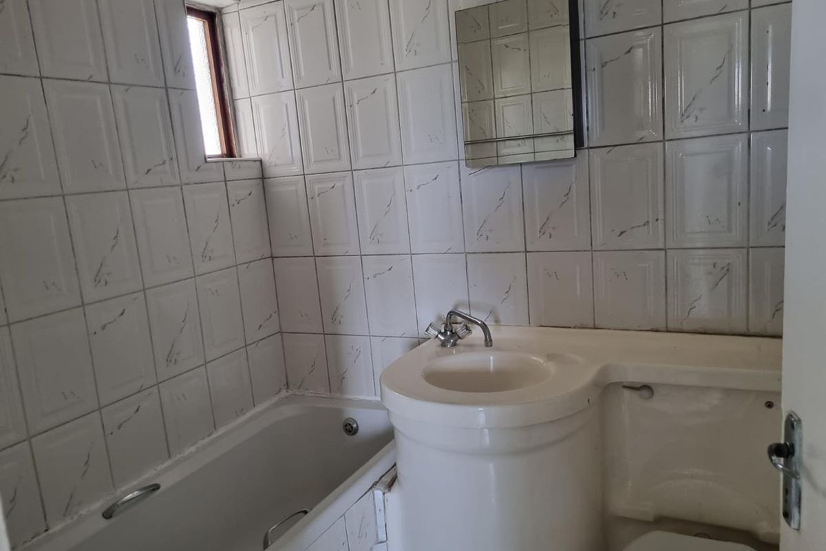 A compact bathroom featuring a built-in bathtub, integrated vanity basin, and wall-mounted mirror cabinet with classic white tiled walls.