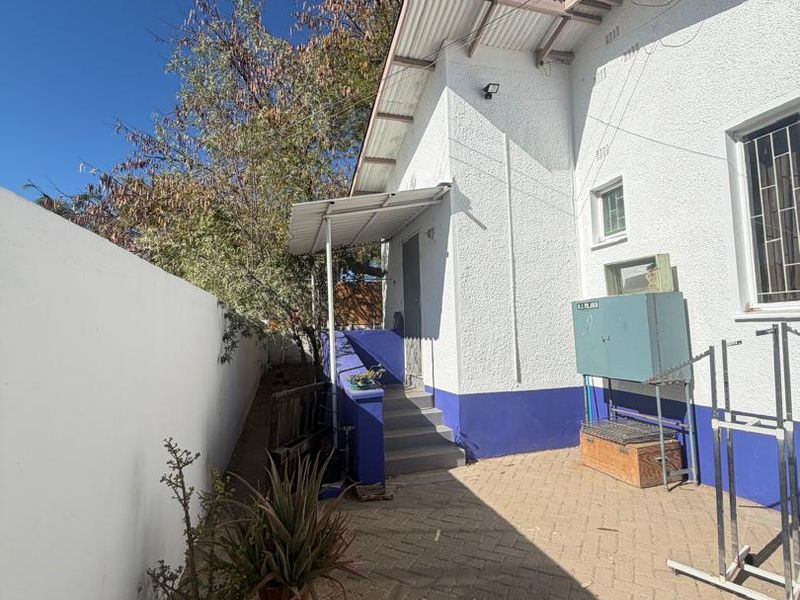Rear exterior view of the property featuring a paved courtyard, boundary wall, and external staircase leading to a side entrance.