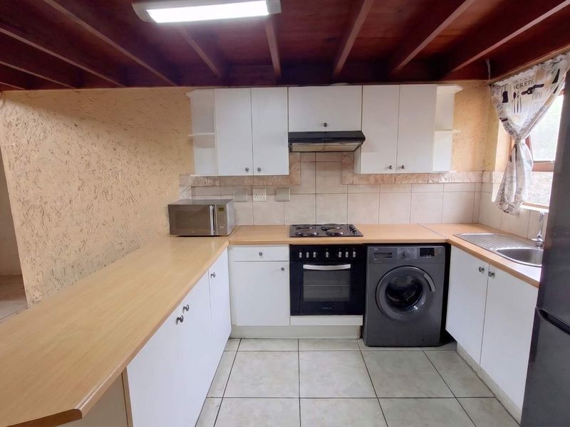 Functional kitchen featuring white cabinetry, laminate countertops, built-in oven, electric hob, and exposed timber ceiling beams with tiled flooring.