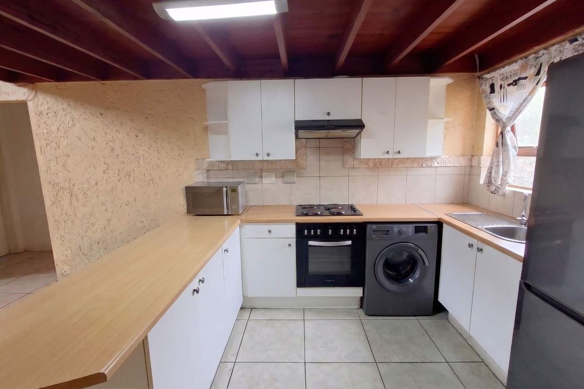 Functional kitchen featuring white cabinetry, laminate countertops, built-in oven, electric hob, and exposed timber ceiling beams with tiled flooring.