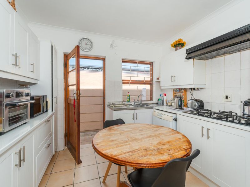 A functional kitchen featuring white cabinetry, a gas hob with extractor fan, tiled flooring, and direct access to an outdoor area.