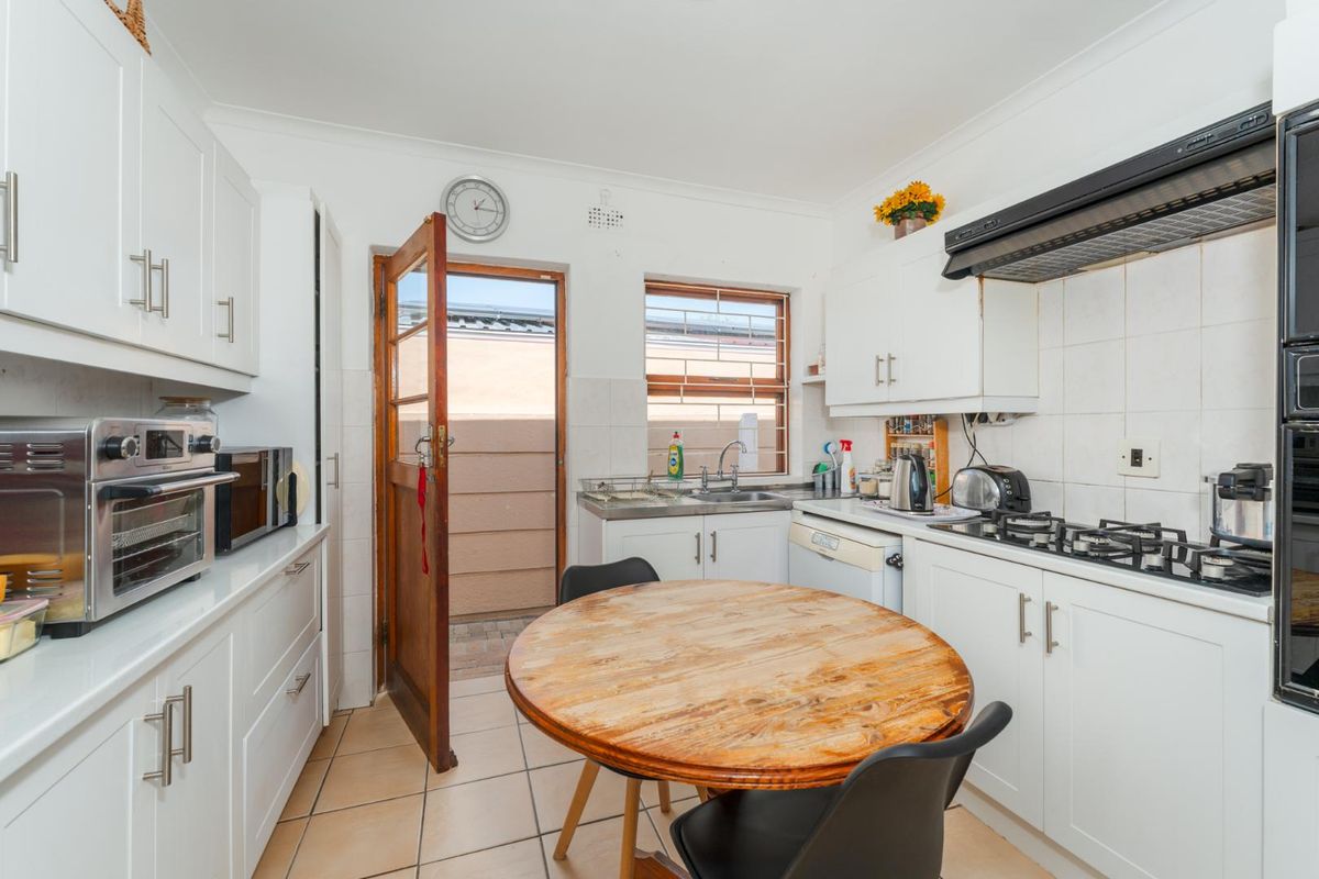 A functional kitchen featuring white cabinetry, a gas hob with extractor fan, tiled flooring, and direct access to an outdoor area.