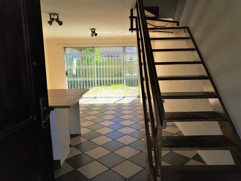 Open plan living area featuring a staircase, tiled flooring, and a security gate leading to the outdoor space.