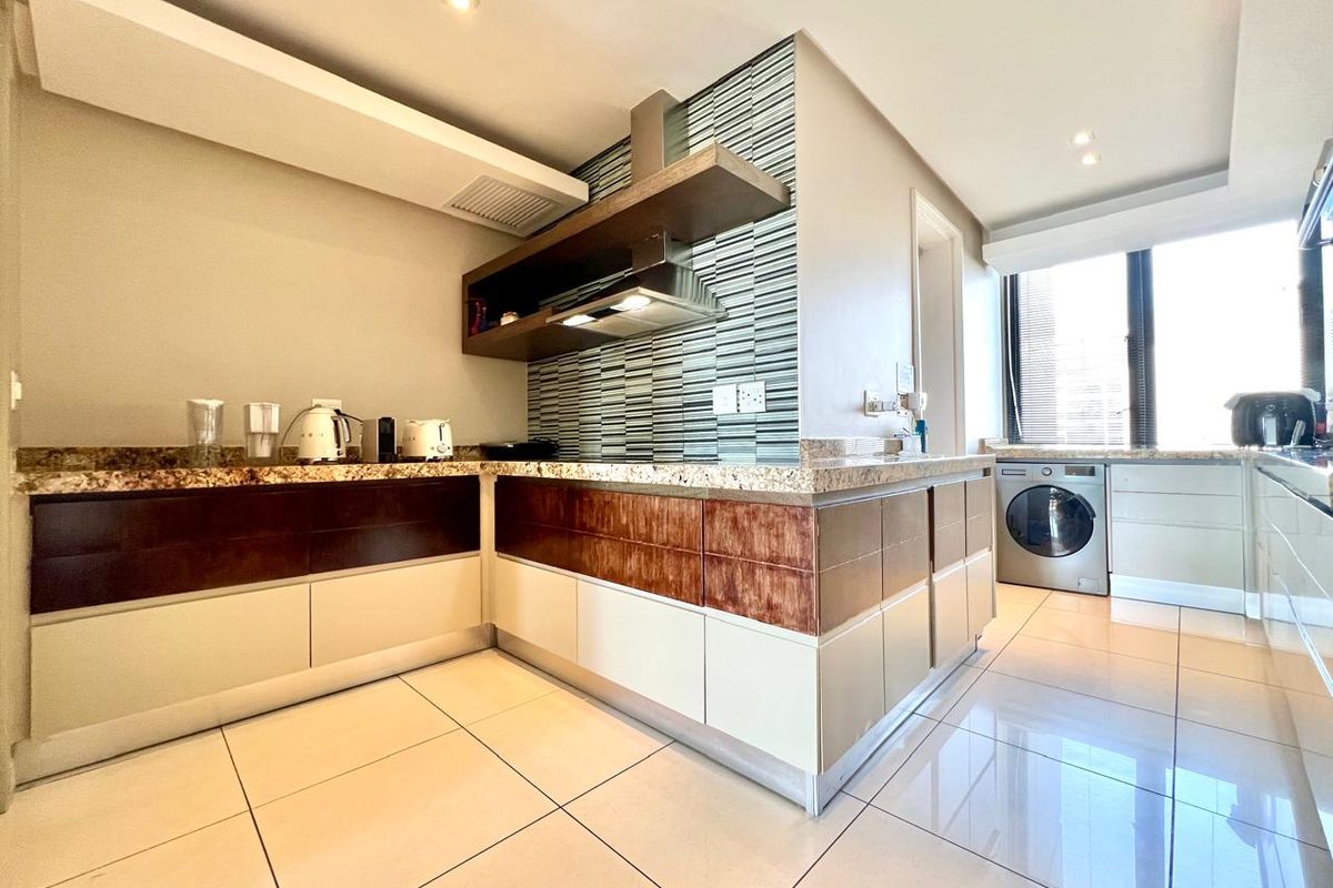 Modern kitchen featuring granite countertops, mosaic tile backsplash, built-in cabinetry, and integrated laundry space with tiled flooring and recessed lighting.