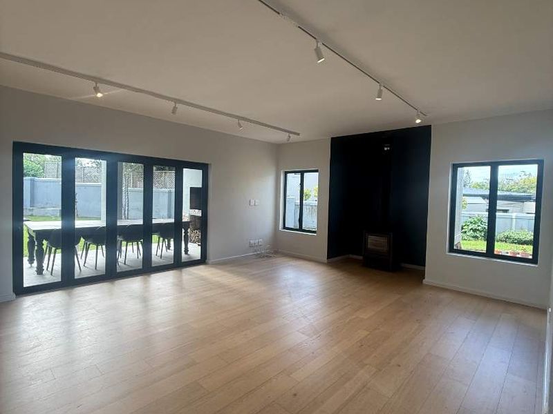 Spacious living room featuring light hardwood flooring, modern track lighting, a sleek freestanding fireplace, and large bi-fold doors opening to the garden.