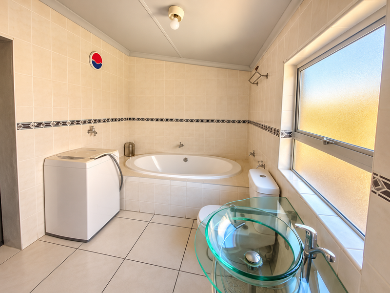 A functional bathroom featuring a built-in bathtub, tiled finishes, a frosted glass window, and a modern glass vessel sink.