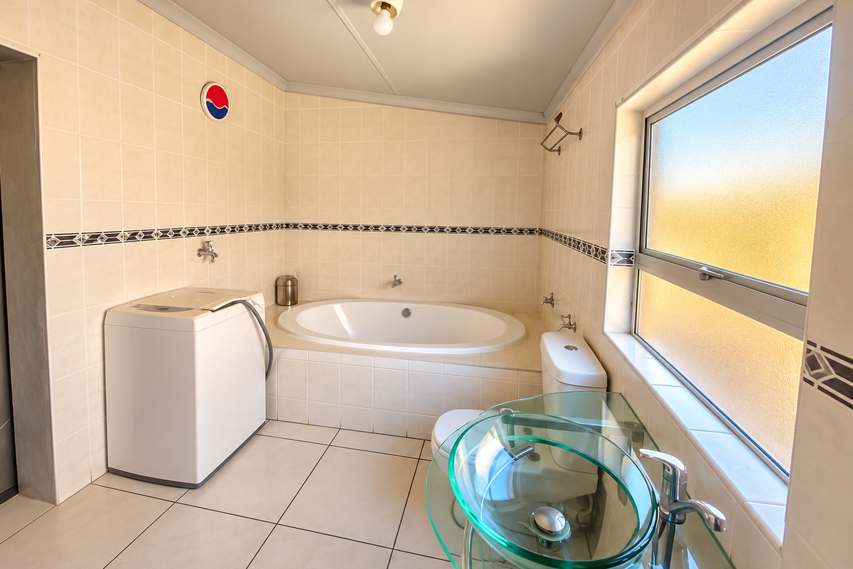 A functional bathroom featuring a built-in bathtub, tiled finishes, a frosted glass window, and a modern glass vessel sink.